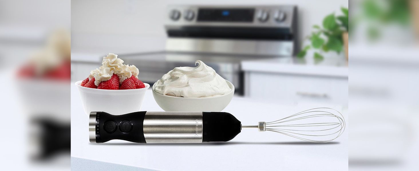 Hand blender with whisk on a white counter in front of two bowls of strawberries and whipped cream