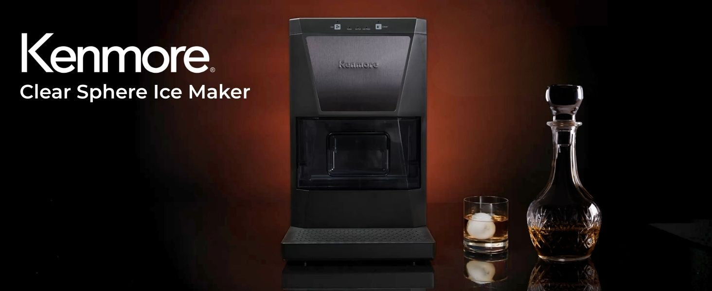 Kenmore clear sphere ice maker on a dark black and brown background with a crystal decanter and glass to the right filled with clear amber liquid. Text overlay reads, "Kenmore clear sphere ice maker."