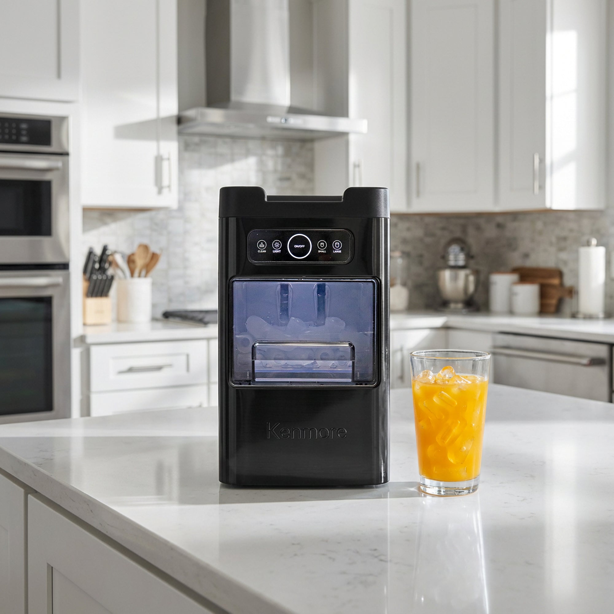 Kenmore automatic front-load ice maker on a light wooden countertop with a person pouring lemonade into glasses filled with ice in the background