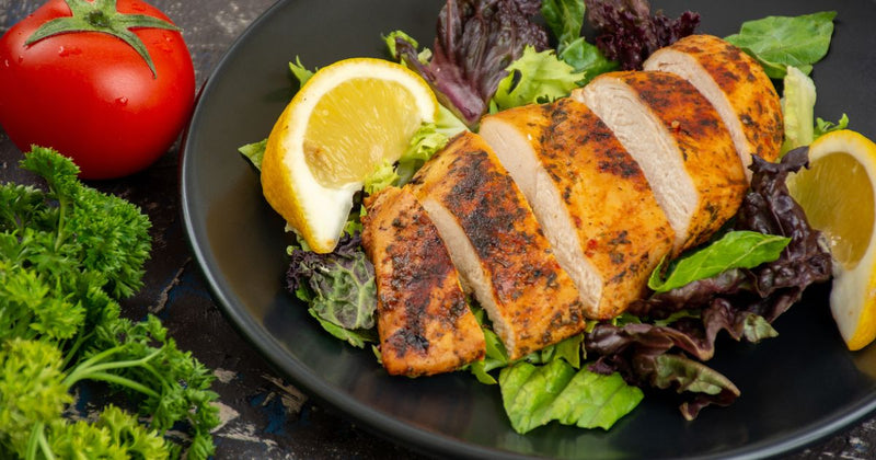 Photo of a sliced cooked chicken breast on a bed of spring greens with lemon wedges on either side