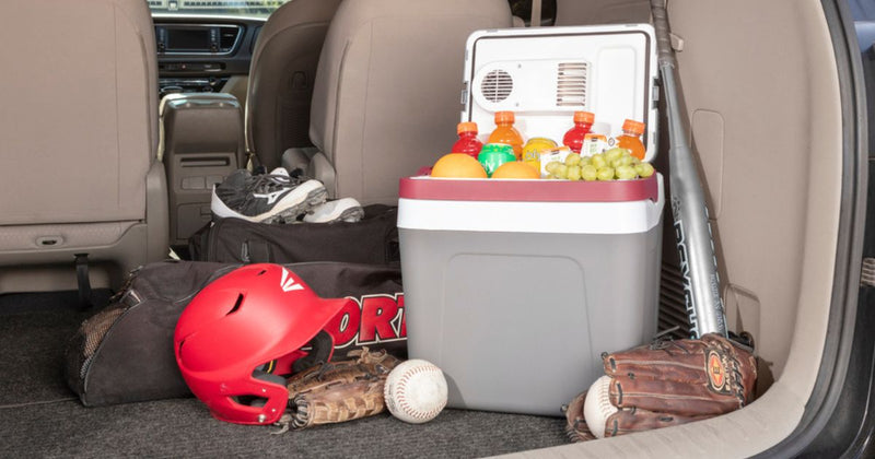Photo of an open gray and white cooler filled with food and drinks in the back of a van with sports equipment around it