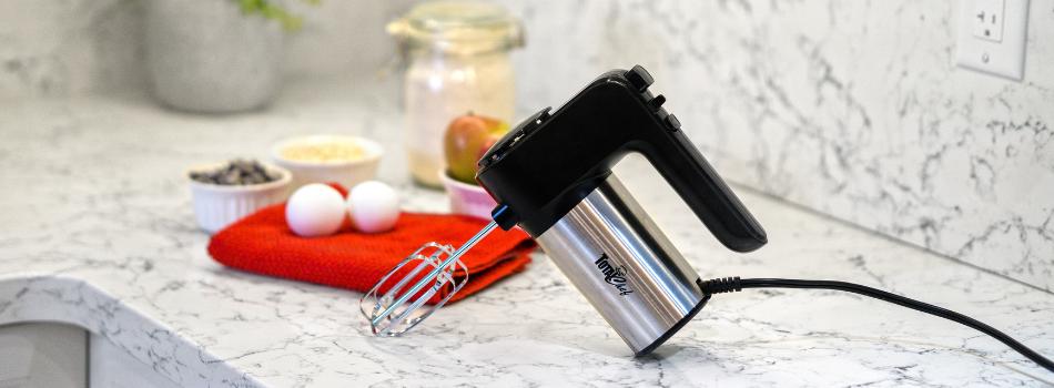 Black and stainless steel hand mixer on a white and gray marble countertop