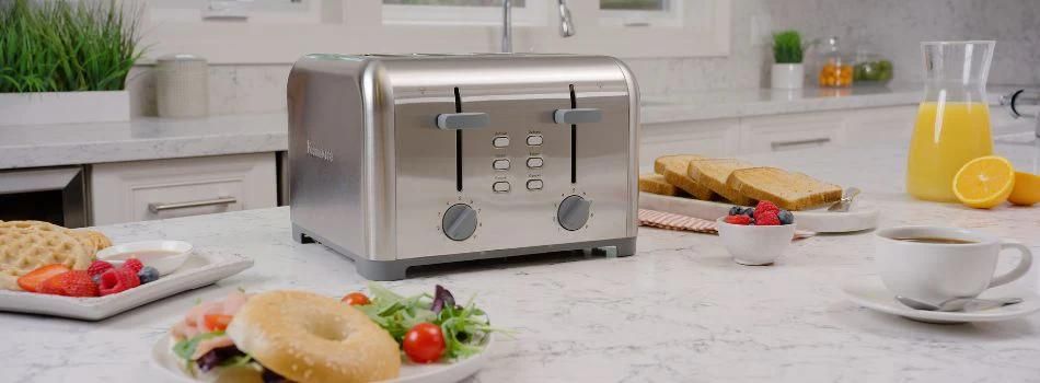 Stainless steel four slice toaster on a white marble counter surrounded by breakfast foods