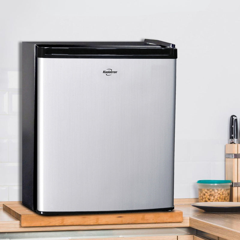 Black and stainless steel compact fridge on a light colored wooden countertop with a white tile wall behind