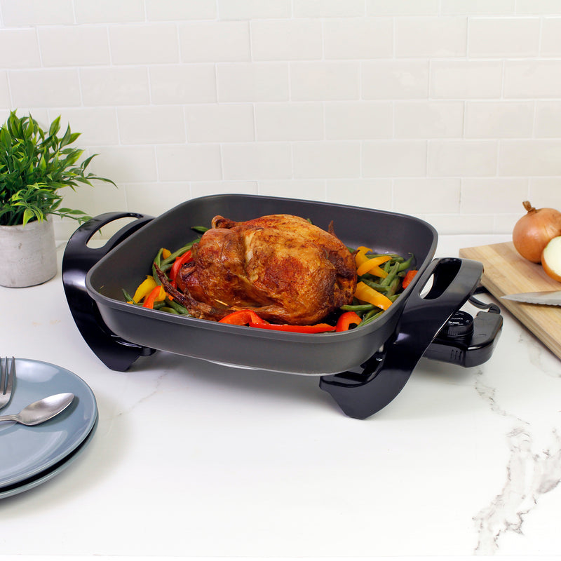 Kenmore non-stick electric skillet with a whole cooked chicken and sauteed vegetables on a white and gray marble countertop.