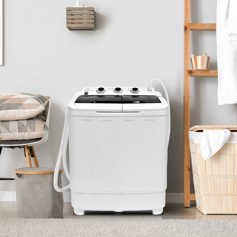 Kenmore twin tub washer and spinner on a beige carpet with a light gray wall behind and laundry hampers, a chair, and a wooden shelf on either side.