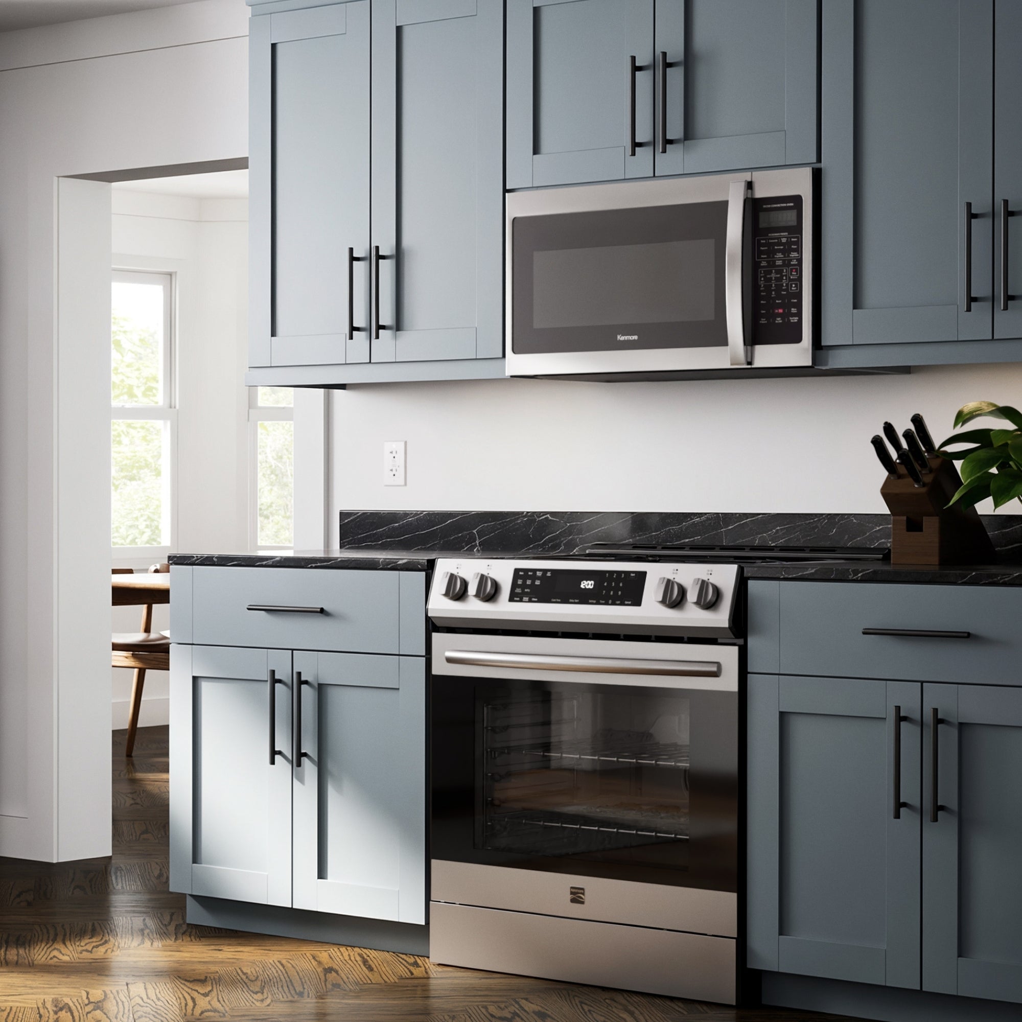Kenmore over-the-range microwave installed in a bright modern kitchen with a stainless steel range and light blue cupboards.
