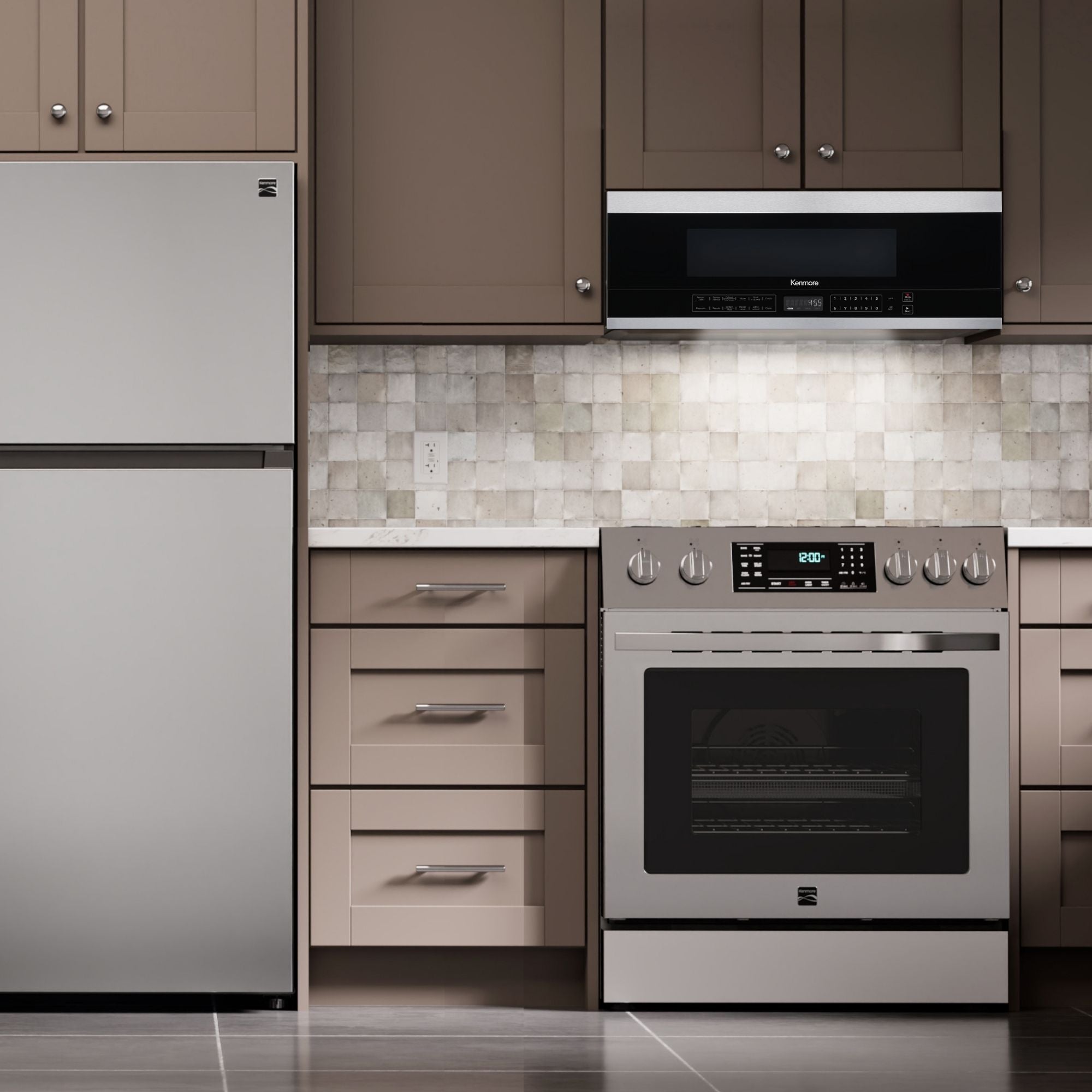 Kenmore over-the-range microwave installed in a taupe kitchen above a stainless steel range with a stainless steel top-mount refrigerator to the left.