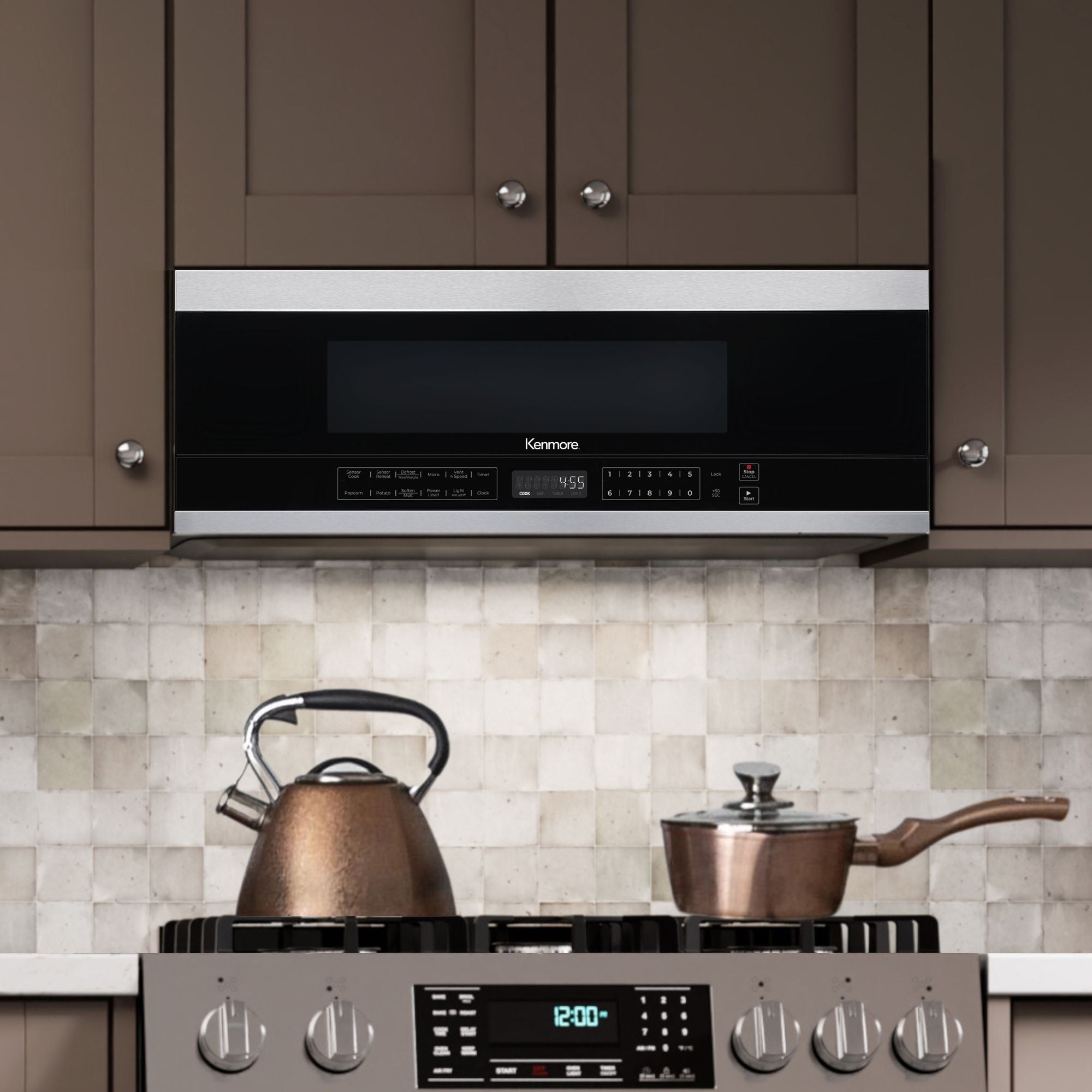 Kenmore over-the-range microwave installed between taupe cupboards. There is a gas range below with a copper pot and kettle on it and a cream tile backsplash behind.