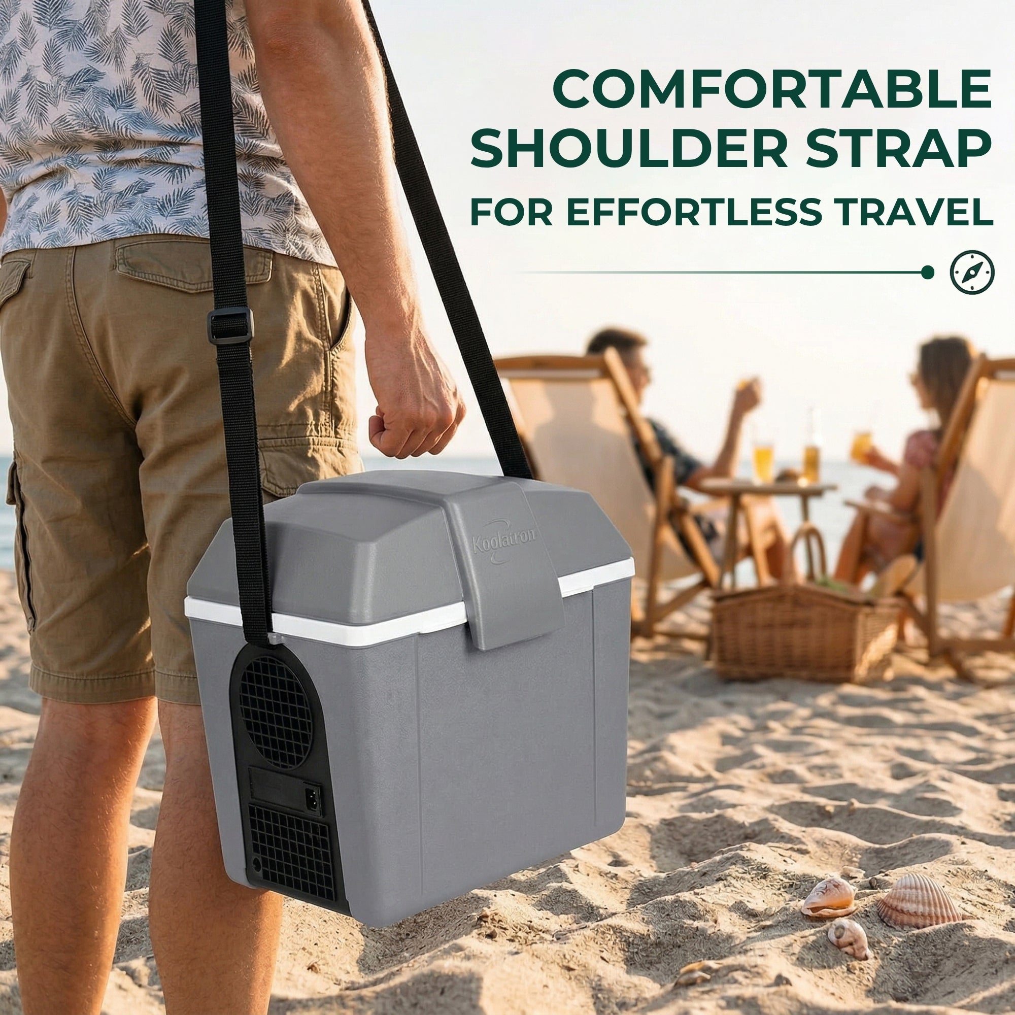Person carrying a 12V cooler/warmer with a shoulder strap on a beach, with people sitting and enjoying a picnic in the background.