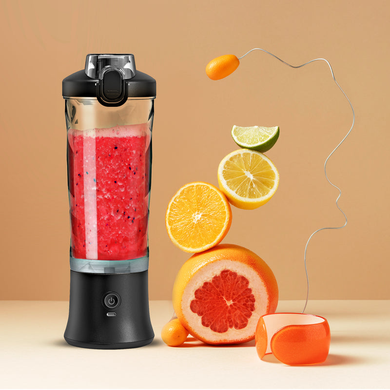 Lifestyle image of the Total Chef USB chargeable blender filled with bright red smoothie on a light orange-yellow background with a stack of sliced citrus fruit beside it.