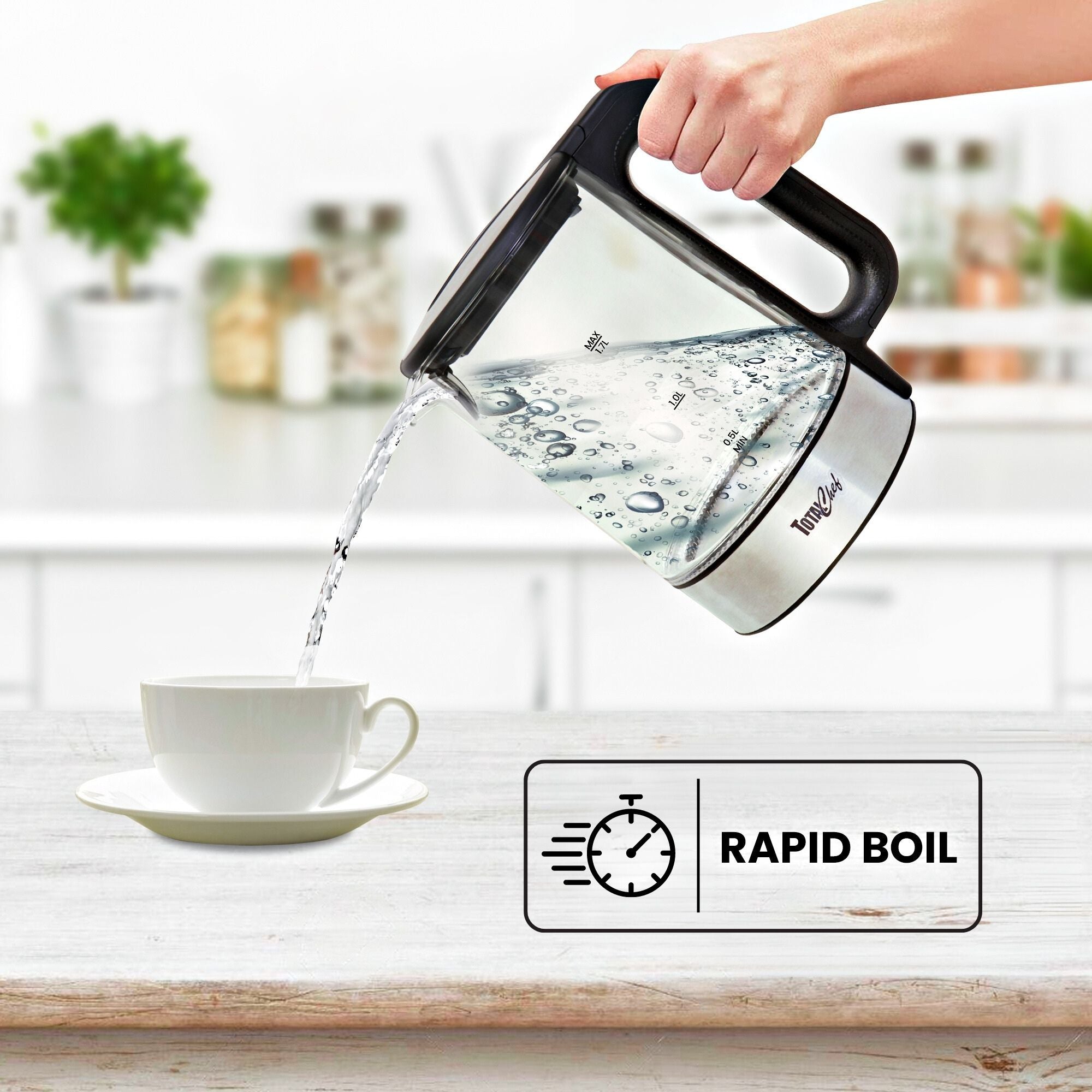 A person's hand lifting the cordless kettle and pouring boiling water into a white teacup on a saucer on a rustic wooden table with a kitchen counter in the background. Text overlay reads, "Rapid boil"