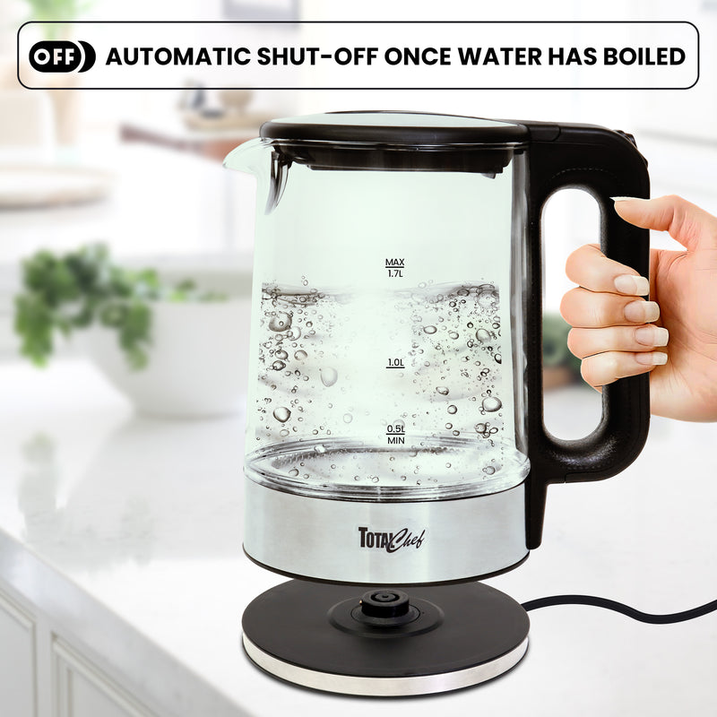 Hand lifting glass kettle with boiling water off the base on a white kitchen counter. Text above reads, "Automatic shut-off once water has boiled"