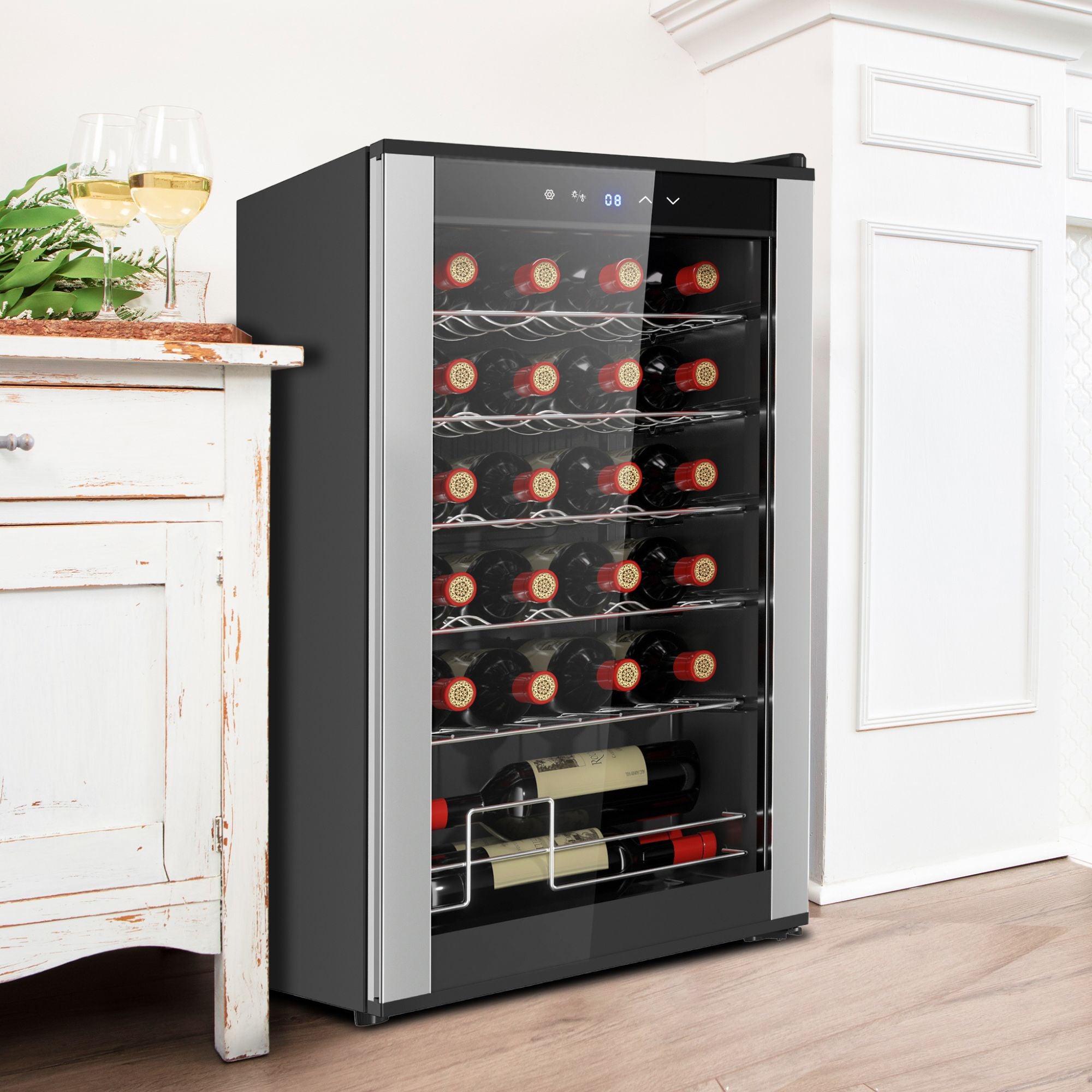 Koolatron 24 bottle freestanding compressor wine fridge, closed, set up between a white end table with two glasses of white wine on it and a white mantle