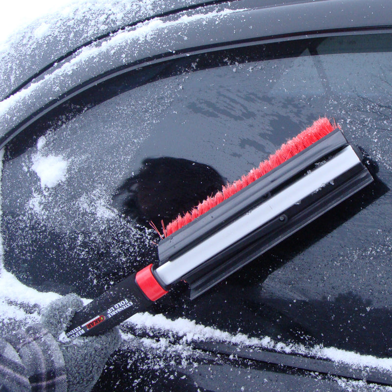 Lifestyle image of a gloved hand using the snow brush with the head doubled up to brush snow from the window of a dark coloured car