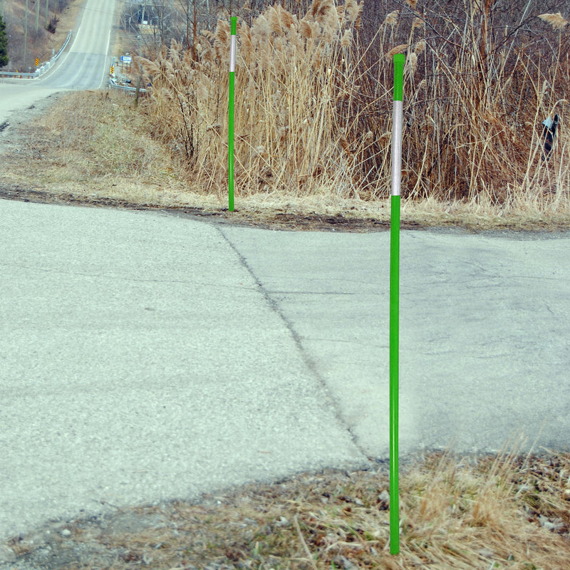 Lifestyle image of two green driveway markers installed in the grass on either side of the entrance of a paved driveway coming off two-lane road