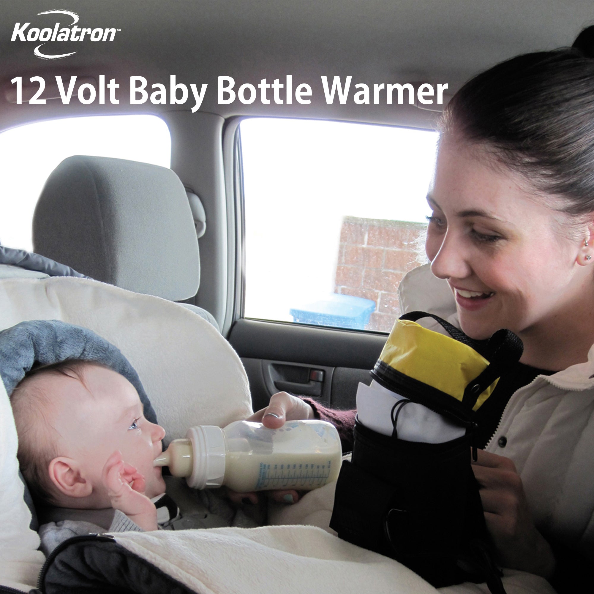 Lifestyle image of a person with light skin and brown hair in a ponytail feeding a bottle of milk to an infant with light skin sitting in a car seat. Text overlay reads, "Koolatron 12V baby bottle warmer"