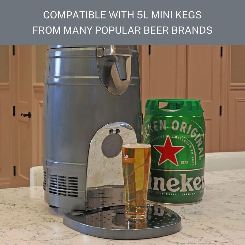 Lifestyle image of 5 liter mini-keg dispenser on a white and black marble countertop with a full glass of beer positioned below the spout, a green 5L mini keg with a red star design to the right, and light tan cupboards in the background. Text above reads, "Compatible with 5L mini kegs from many popular beer brands."