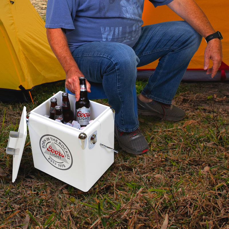 Lifestyle image of a person wearing jeans and a blue t-shirt sitting in front of two yellow dome tents and lifting a bottle of Coors Light beer out of the open ice chest