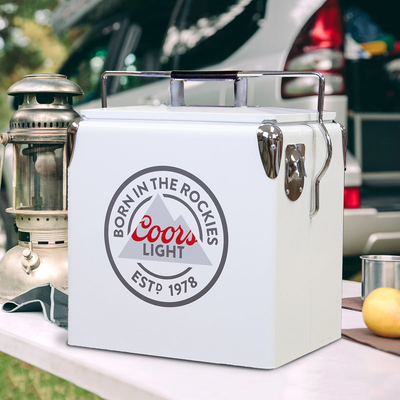 Lifestyle image of Coors Light retro ice chest with bottle opener on a white folding table with a metal lantern beside it and a vehicle in the background