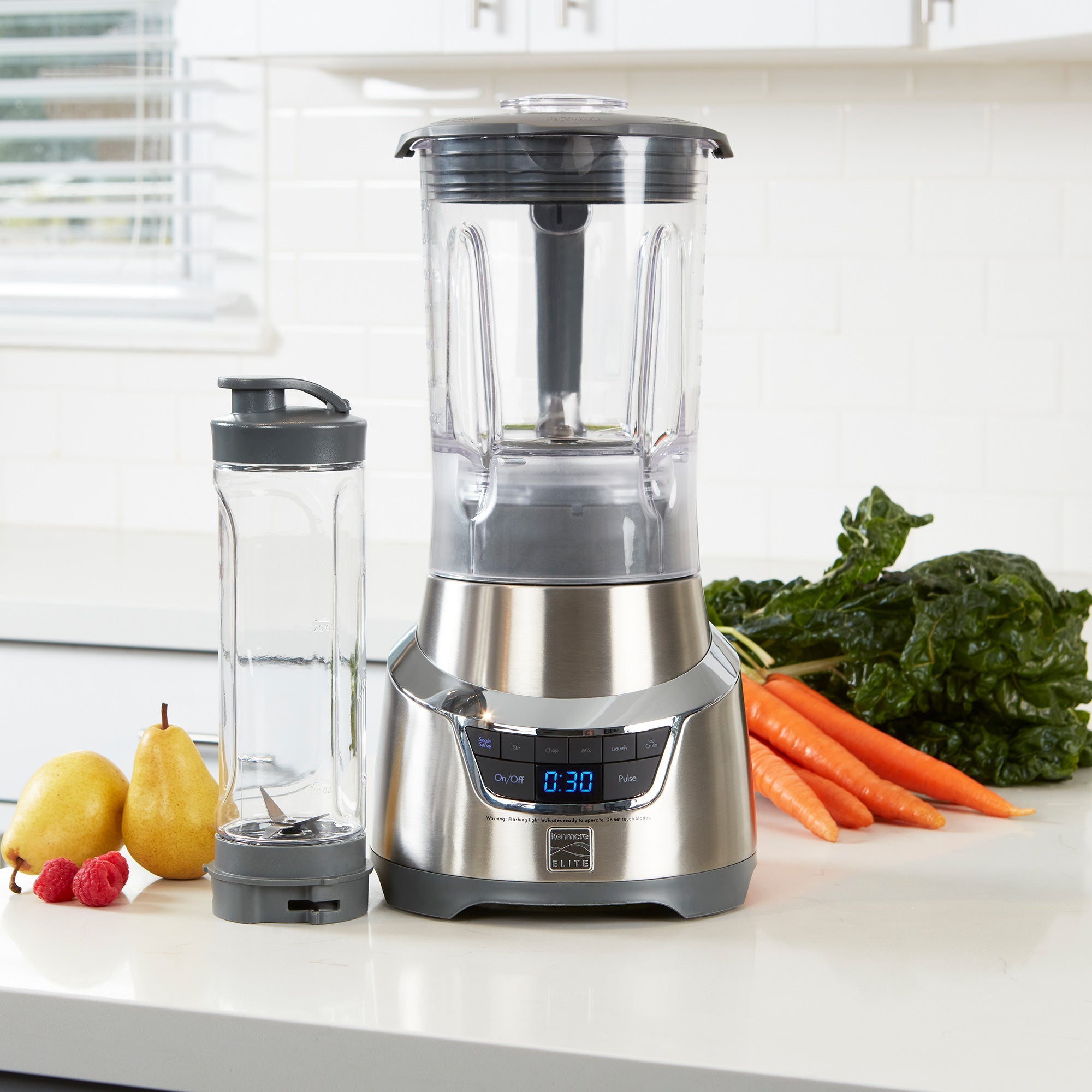 Kenmore Elite 1.3 horsepower blender and travel blending cup empty on white counter with fruits and vegetables on either side