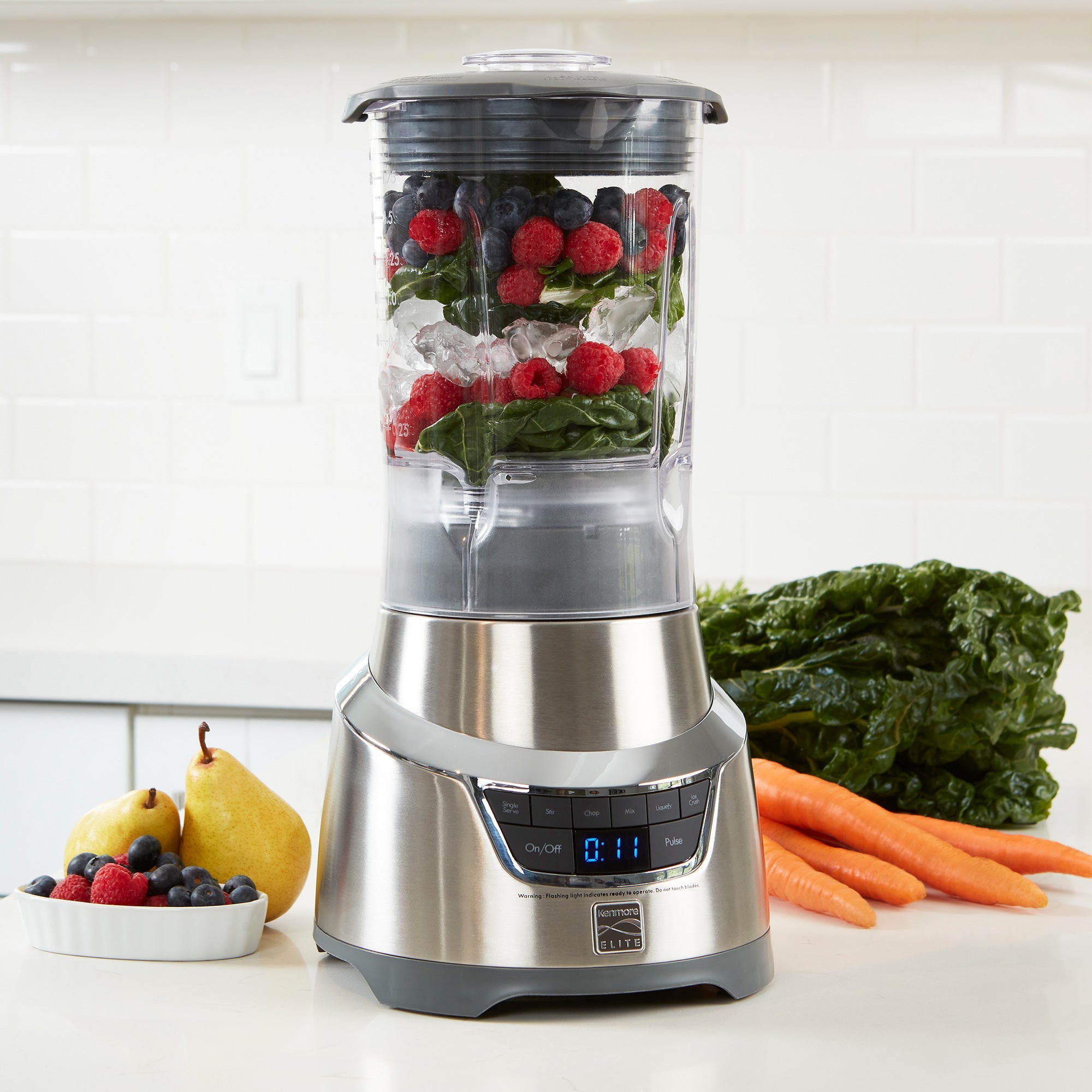 Kenmore Elite blender on white counter with layers of ice and berries ready to blend in the pitcher and fruits and vegetables on either side