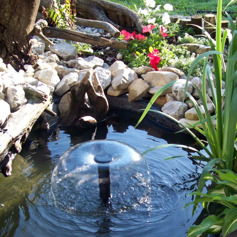 Lifestyle image of a small in ground pond surrounded by plants and stones with a water bell fountain in the middle
