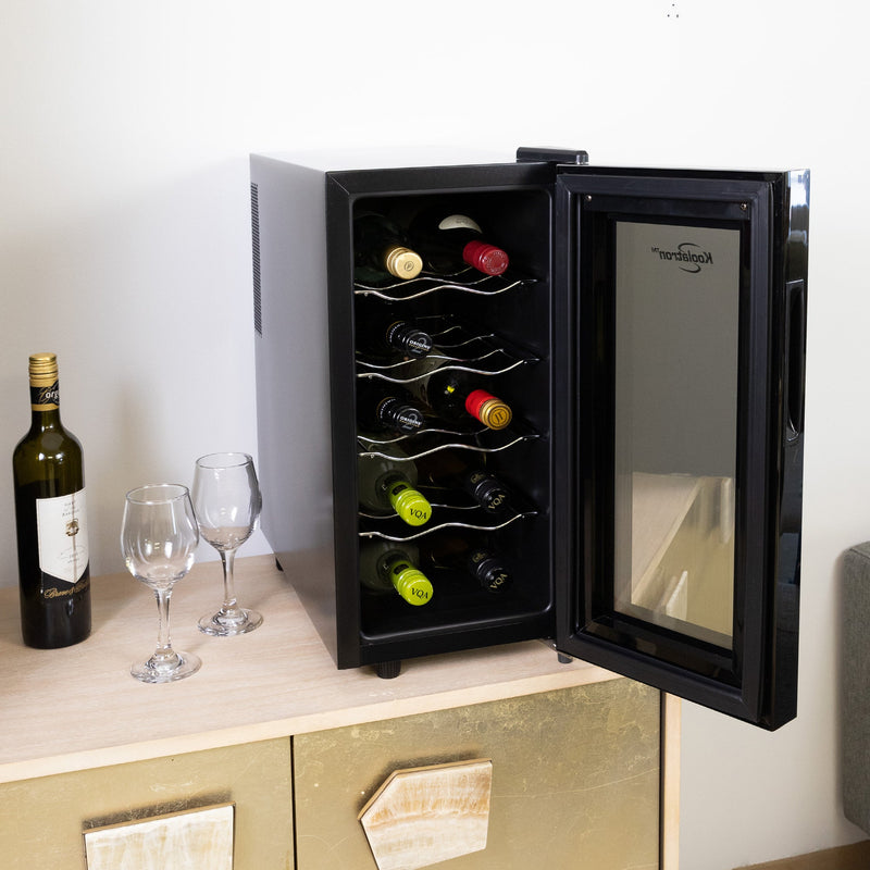 Koolatron 10 bottle wine cooler, open and filled with bottles of wine, on a gold-colored sideboard beside a gray sofa. There is a bottle of wine and two glasses to the left of the cooler