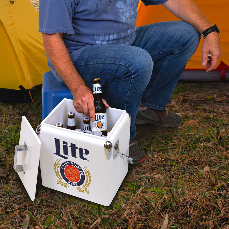 Lifestyle image of a person wearing jeans and a blue t-shirt sitting in front of two yellow dome tents and lifting a bottle of Miller Lite beer out of the open ice chest