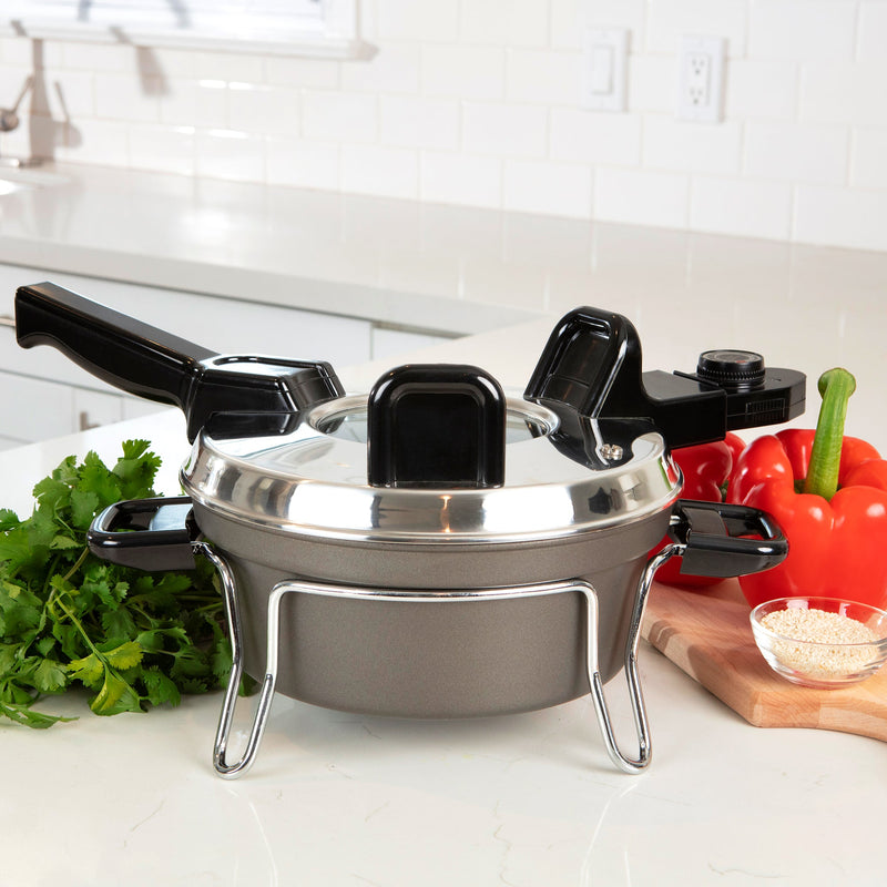 Lifestyle image of Czech cooker with lid on on a light gray countertop with a white tile backsplash. There is a bunch of Italian parsley to the left of the cooker and a cutting board with red peppers and a pinch bowl of salt to the right