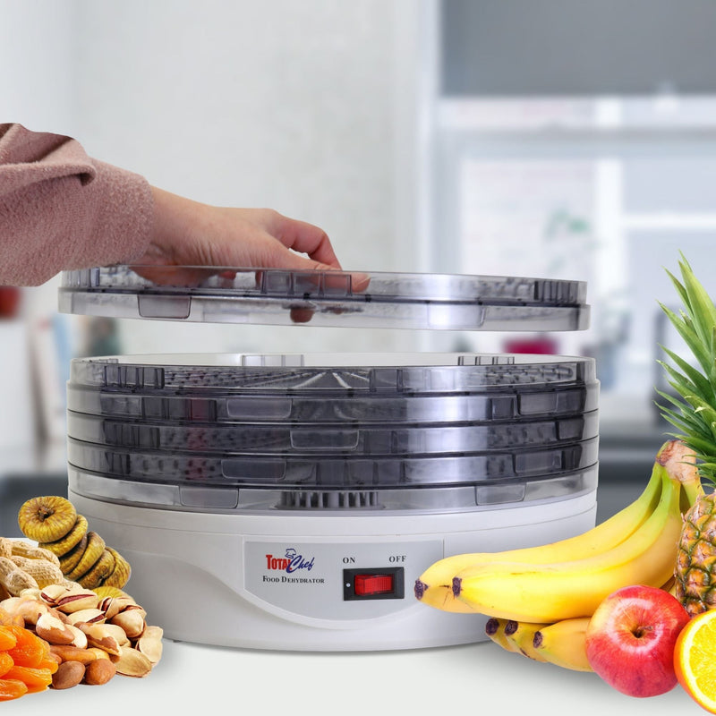 Lifestyle image of food dehydrator with dried and fresh fruits beside it and a person's hand placing the lid on top