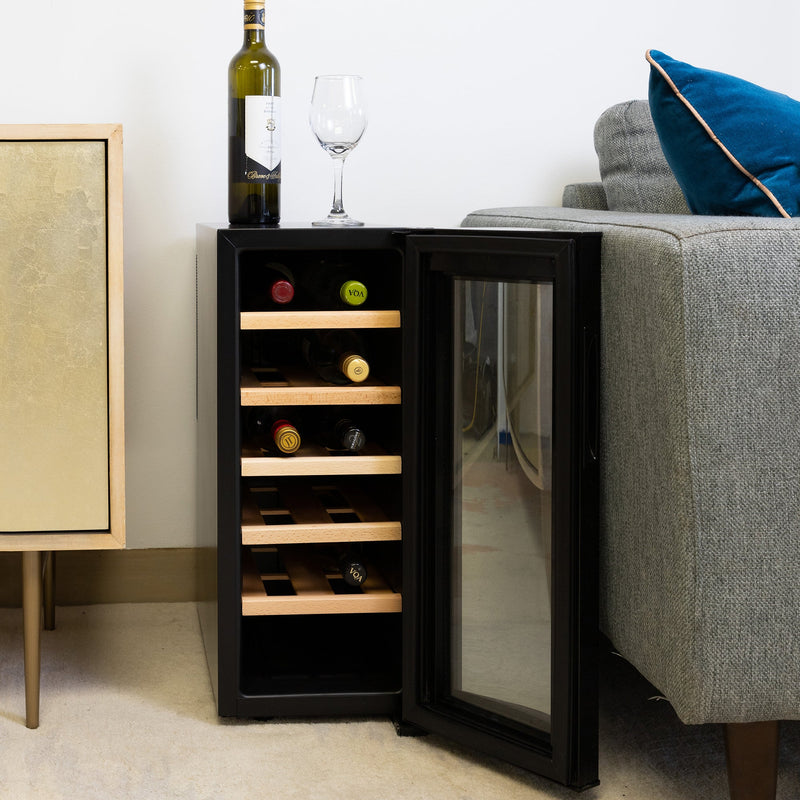 Koolatron 12 bottle wine cooler, open and filled with bottles of wine, between a gray sofa and a gold-coloured sideboard with a bottle of wine and one glass on top