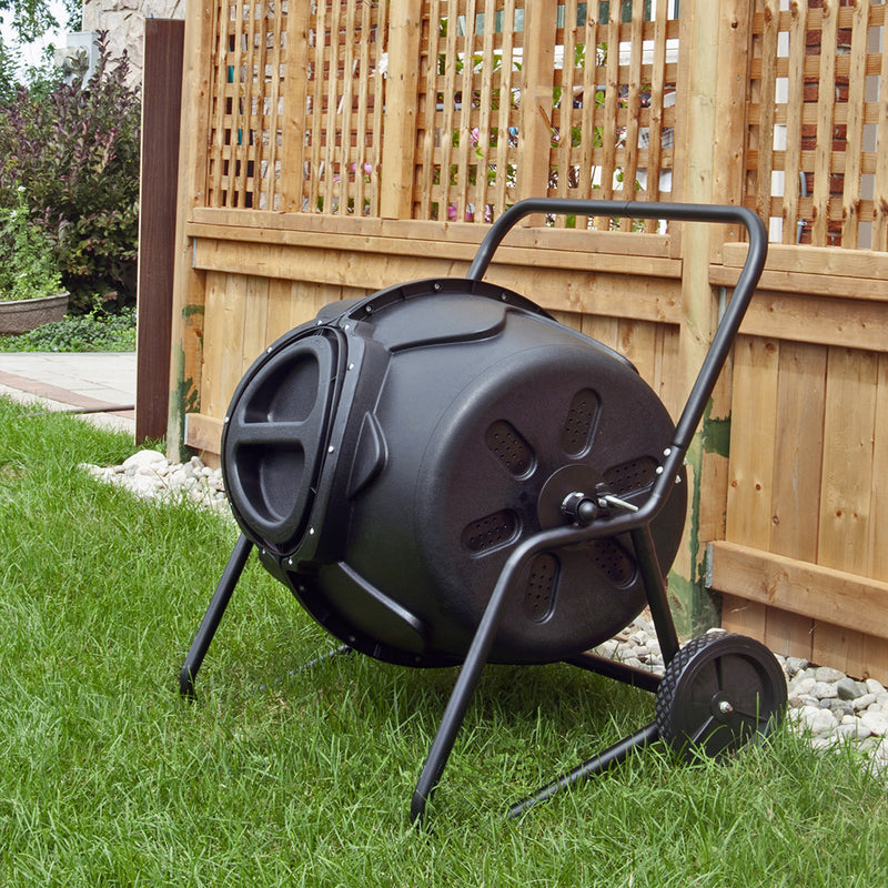 Lifestyle image of wheeled tumbling composter set up on green grass with light-colored wood fence behind it