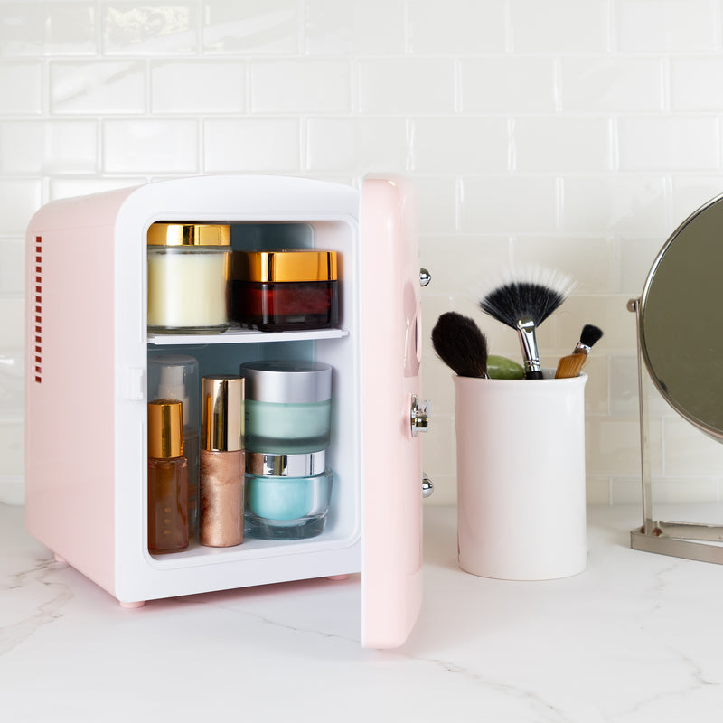 Lifestyle image of Koolatron retro 6 can mini fridge, open with cosmetics and skincare products inside, with makeup brushes in a white container on its right, on a white marbled counter with a white tile backsplash behind